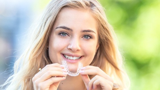 woman smiling while holding Invisalign clear aligner