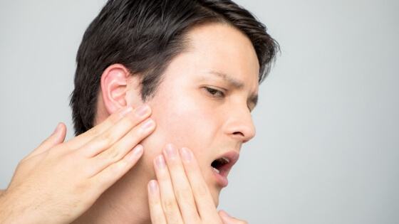 Person experiencing T M J dysfunction holding jaw in pain