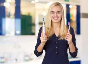 A Woman Holds an Electric and Manual Toothbrush