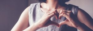 young woman in grey dress making heart symbol with hands