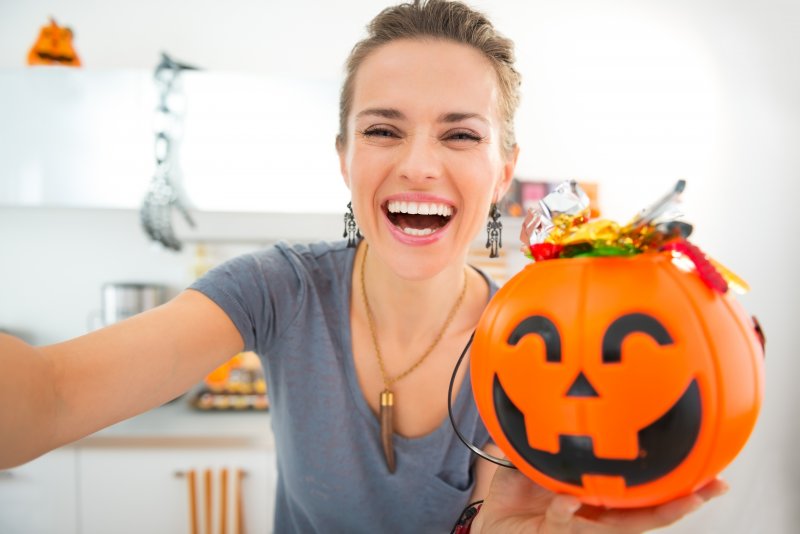 woman smiling while holding Halloween bucket full of candy 